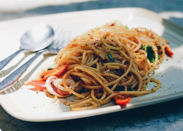 Spaghetti con verdure su piatto quadrato, posate accanto.