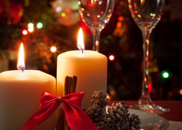 Candele natalizie con fiocchi rossi e calici sullo sfondo.