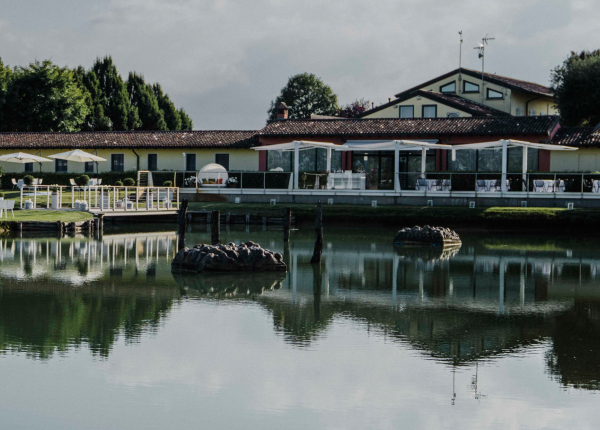 Edificio riflesso in un lago con terrazza e ombrelloni.